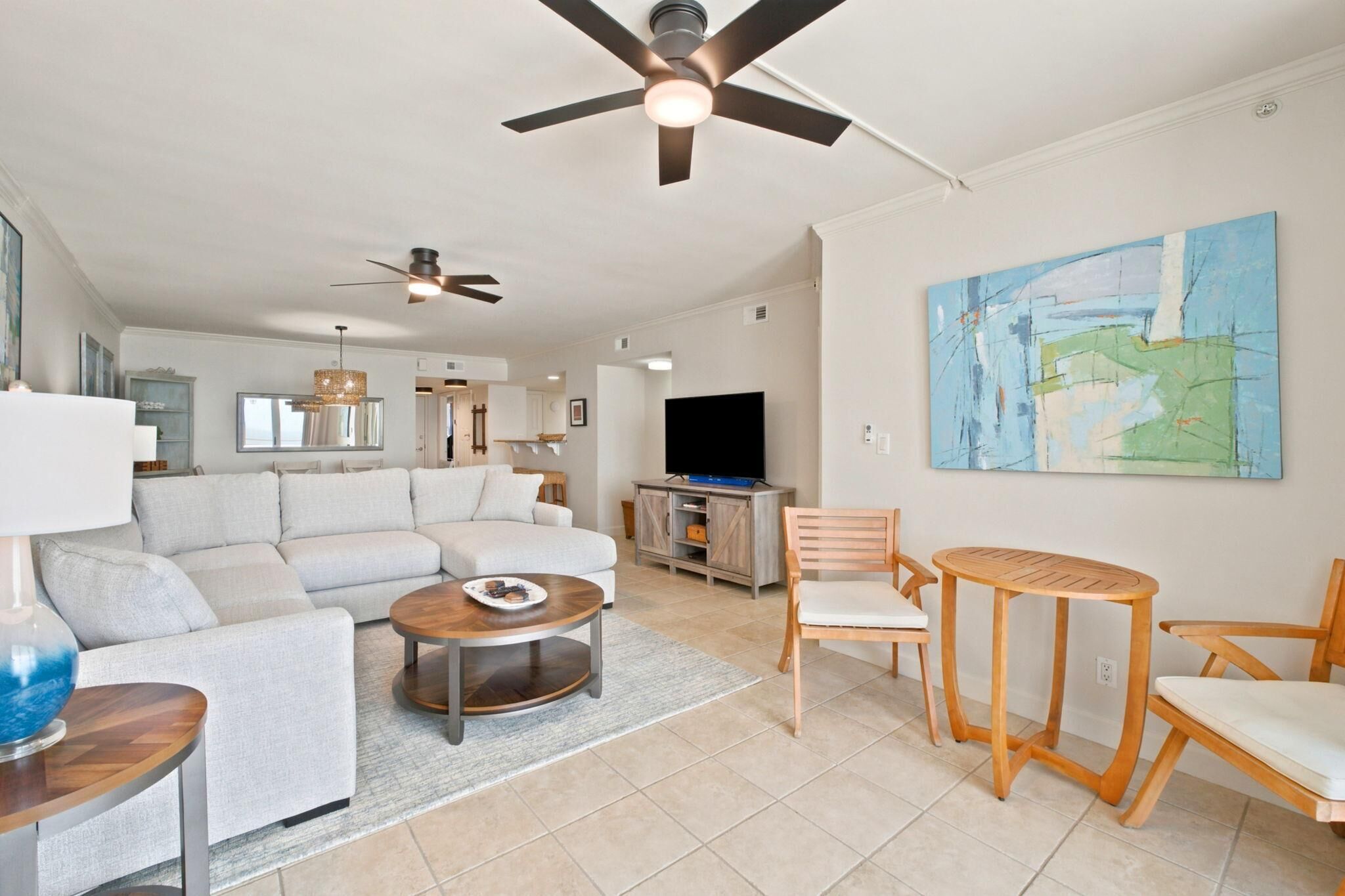 A modern living room with a sofa, coffee table, chairs, a TV, and artwork on the wall.
