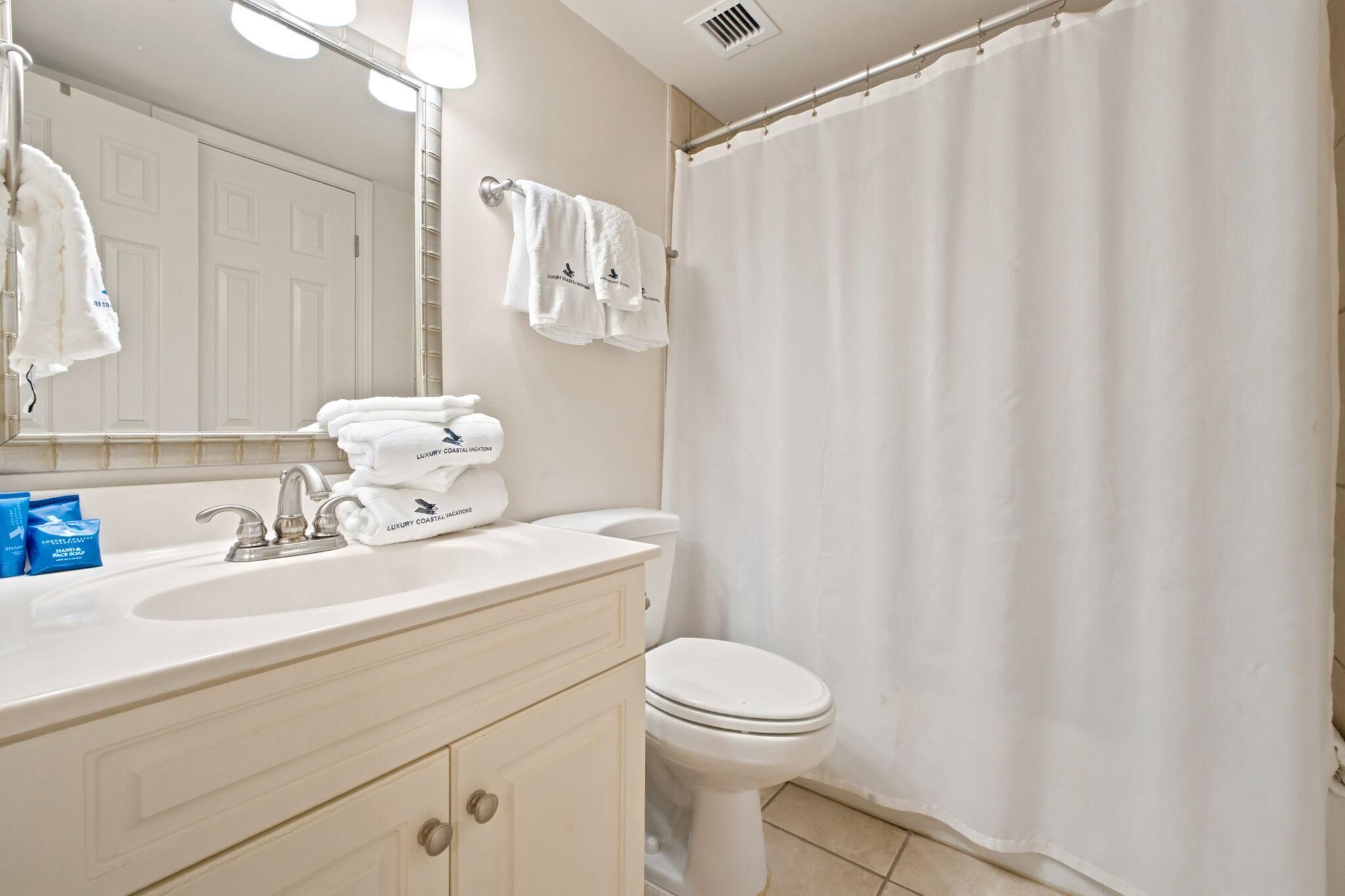 A bathroom with a white sink, vanity, and toilet. There are towels hanging on the wall and a shower curtain.