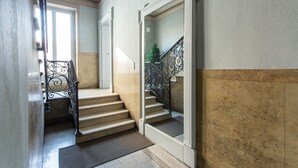 Een trap met een metalen leuning, een deurmat en een deur die naar een andere kamer leidt.
