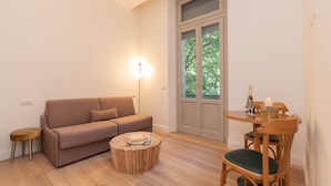 Een woonkamer met een bank, een ronde houten salontafel, een eettafel met stoelen en een vloerlamp.