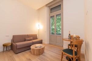 Un salon comprenant un canapé, une table basse ronde en bois, une table à manger avec des chaises et un lampadaire.