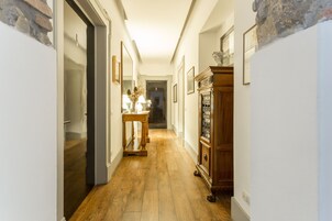 Un couloir doté d’un plancher en bois, une table sur laquelle est posé un vase, et un meuble en bois orné de tableaux encadrés.
