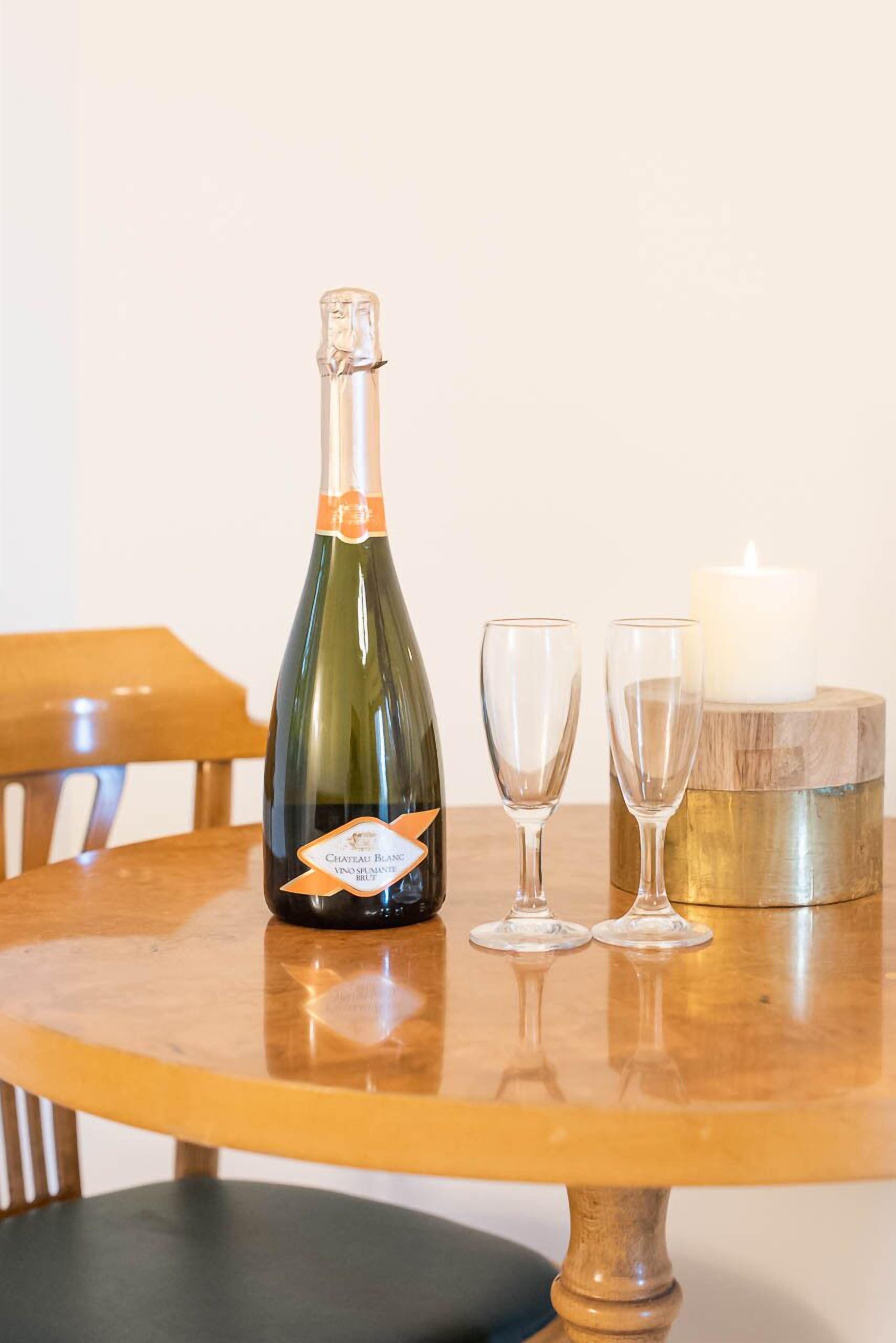 A bottle of Chateau Blanc wine, two glasses, and a candle on a wooden table.
