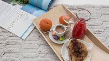 A tray with a croissant, orange, coffee, and a glass of red drink on a textured surface with a book and magazine.