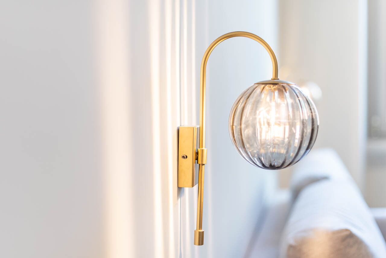 Una lámpara de pared con pantalla de cristal esférica y brazo dorado.