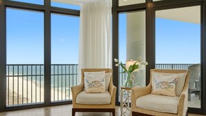 A balcony with two wicker chairs, a vase with flowers, and a view of the beach.