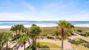 A beachfront property with a paved walkway, palm trees, and a view of the ocean. - Indigo West 301 (Pensacola)