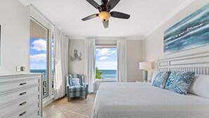 A bedroom with a large bed, a ceiling fan, a view of the ocean, a chair, and a dresser. - Indigo West 301 (Pensacola)