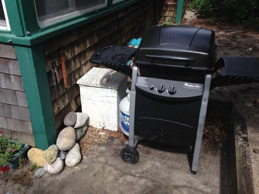 A portable grill with a control panel, a gas canister, and a stack of stones.