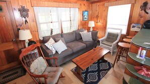 En hyggelig hyttekrog med træloft, sofa, stol, spisebord og lampe.