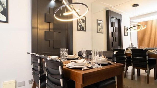 A modern dining area with a wooden table set for four, black chairs, and contemporary pendant lighting. - PRIME LOK- SP FLAT VILA OLIMPIA (São Paulo)
