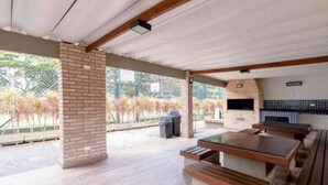 An outdoor patio with a brick column, a barbecue grill, and wooden benches. - PRIME LOK- SP FLAT VILA OLIMPIA (São Paulo)