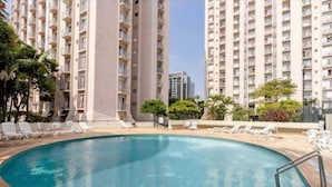 A swimming pool with lounge chairs, surrounded by tall residential buildings. - PRIME LOK- SP FLAT VILA OLIMPIA (São Paulo)