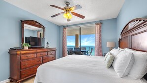 A bedroom with a large bed, a wooden dresser, a ceiling fan, a TV, and a balcony with a view. - Bluewater 1101 (Orange Beach)