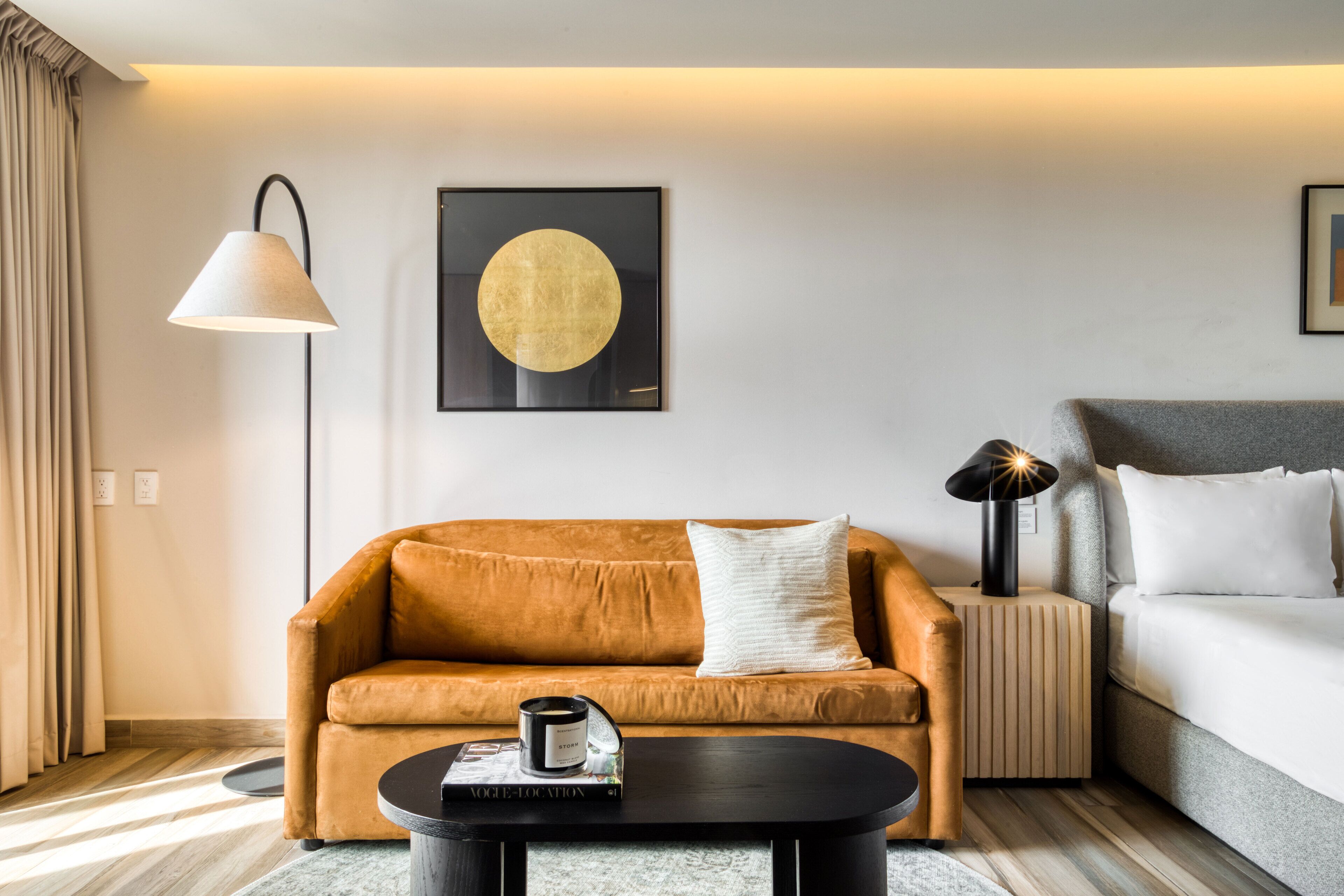 Moderni hotellihuone, jossa on sohva, sohvapöytä, lamppu ja sänky.