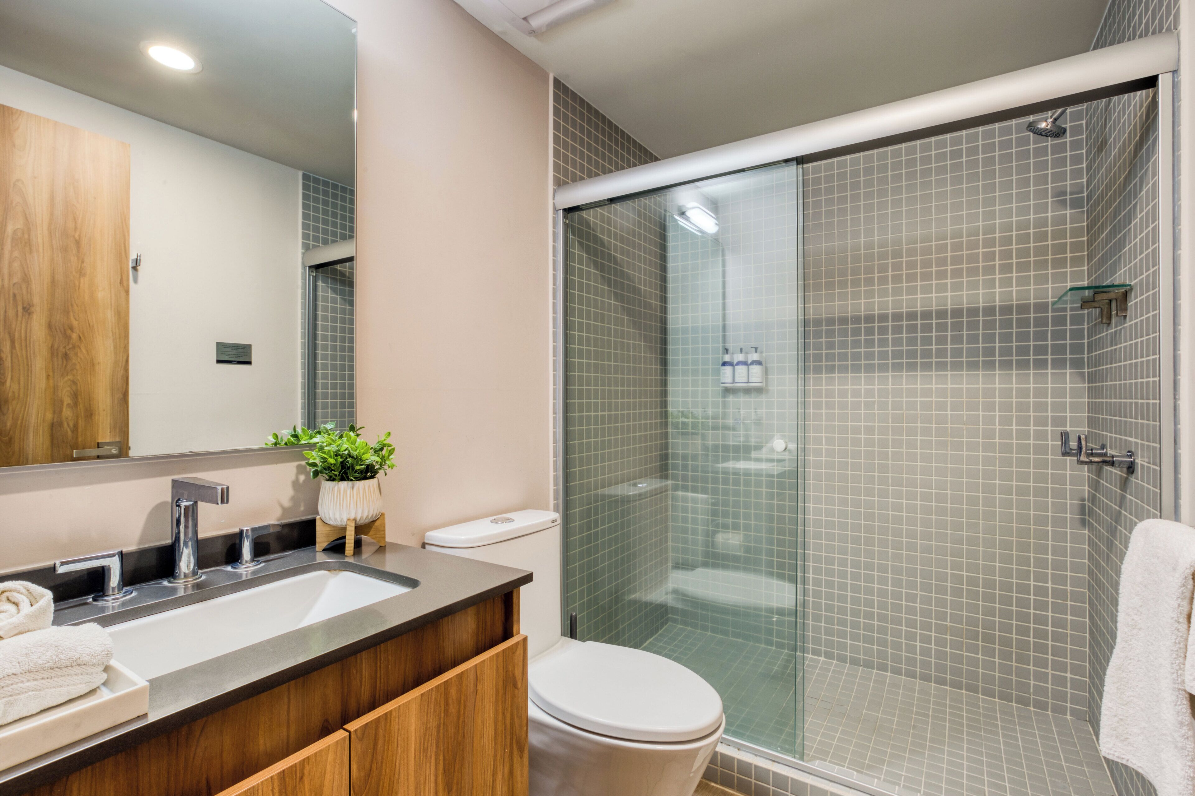 Een moderne badkamer met een wastafel met twee kommen, een toilet en een douche met glazen wanden.