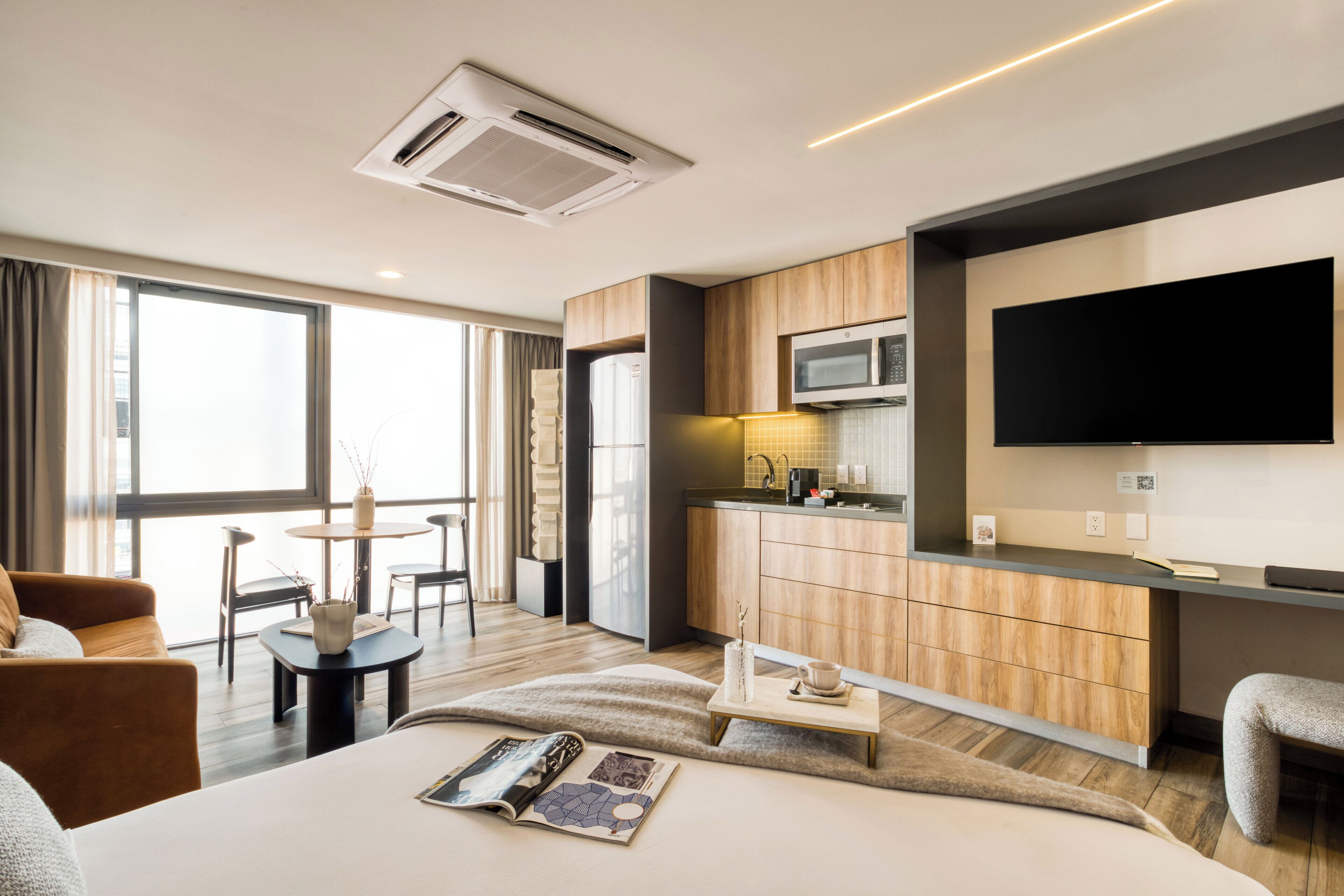 Ein modernes Hotelzimmer mit einem großen Bett, einem Essbereich, einer Küchenzeile und einem an der Wand befestigten Fernseher.