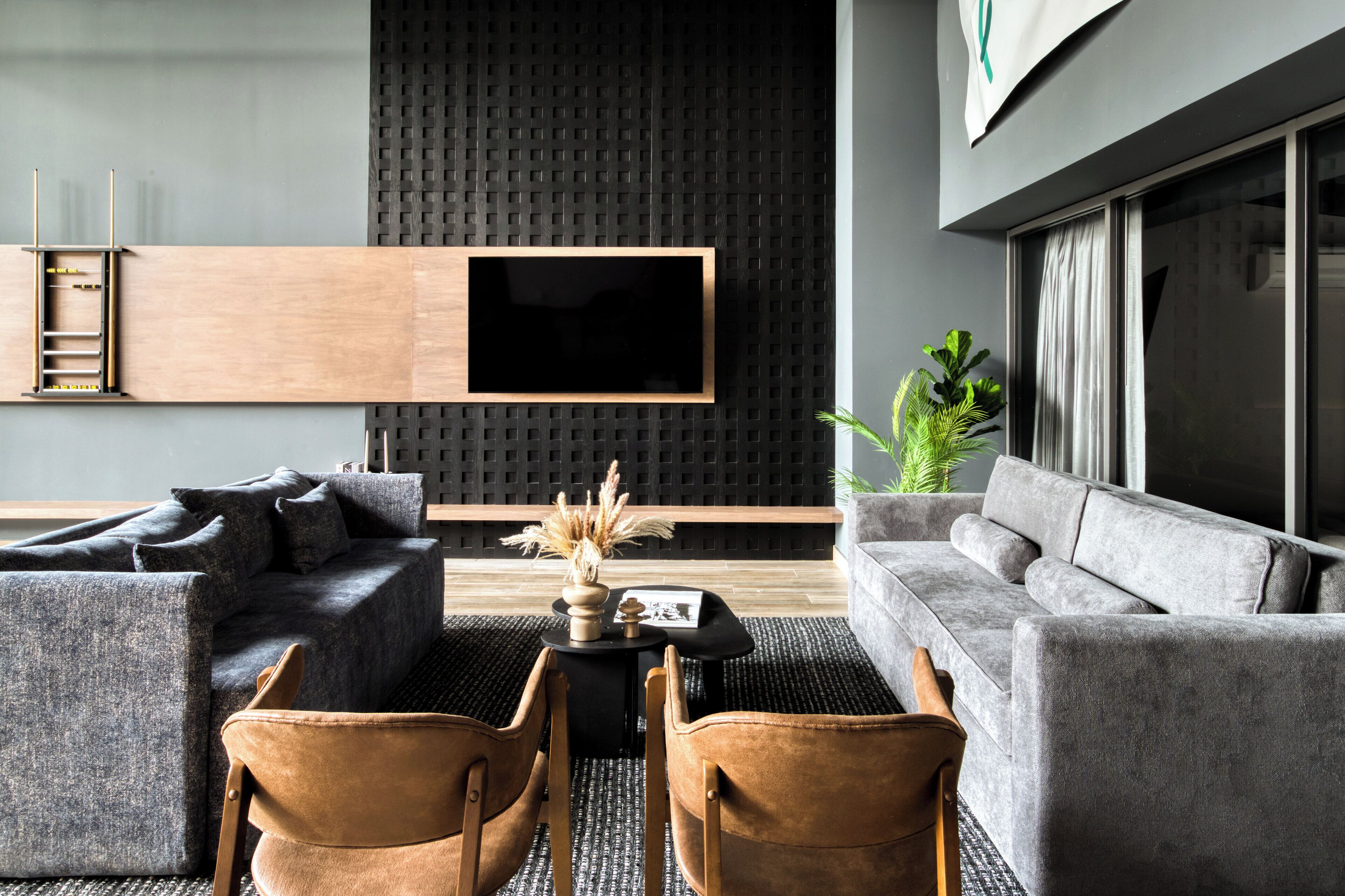 A modern living room with a large flat-screen TV mounted on a textured wall, grey sofas, a coffee table with decorative items, and a plant.