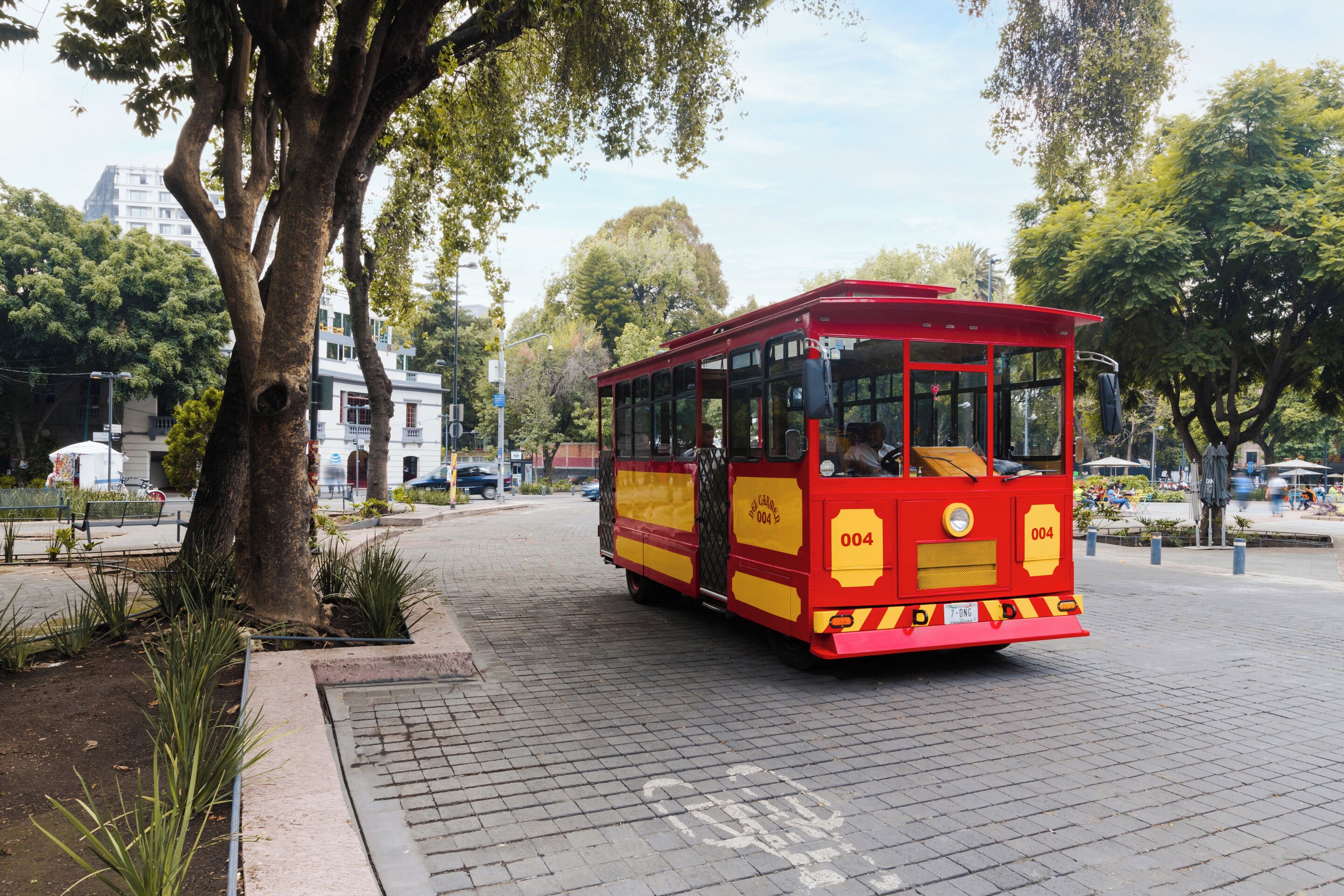 A red trolley with the number 004 on a paved street with trees and buildings in the background.