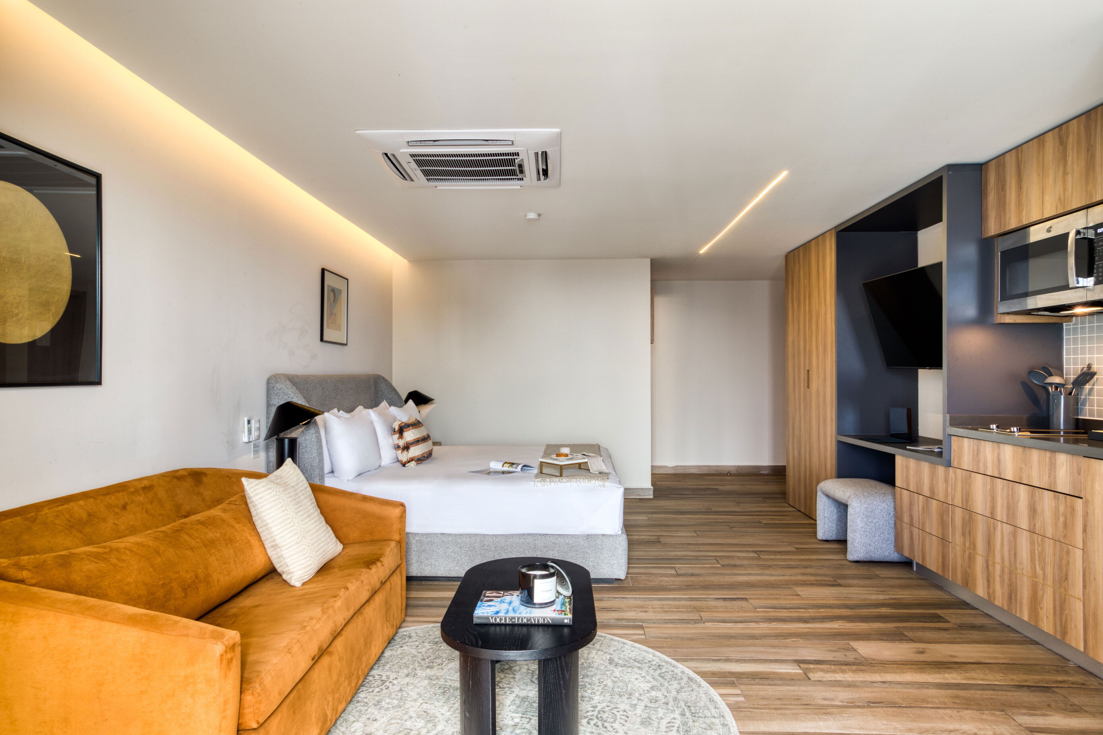 Una habitación de hotel moderna con sofá, cama, una mesita y un kitchenette.