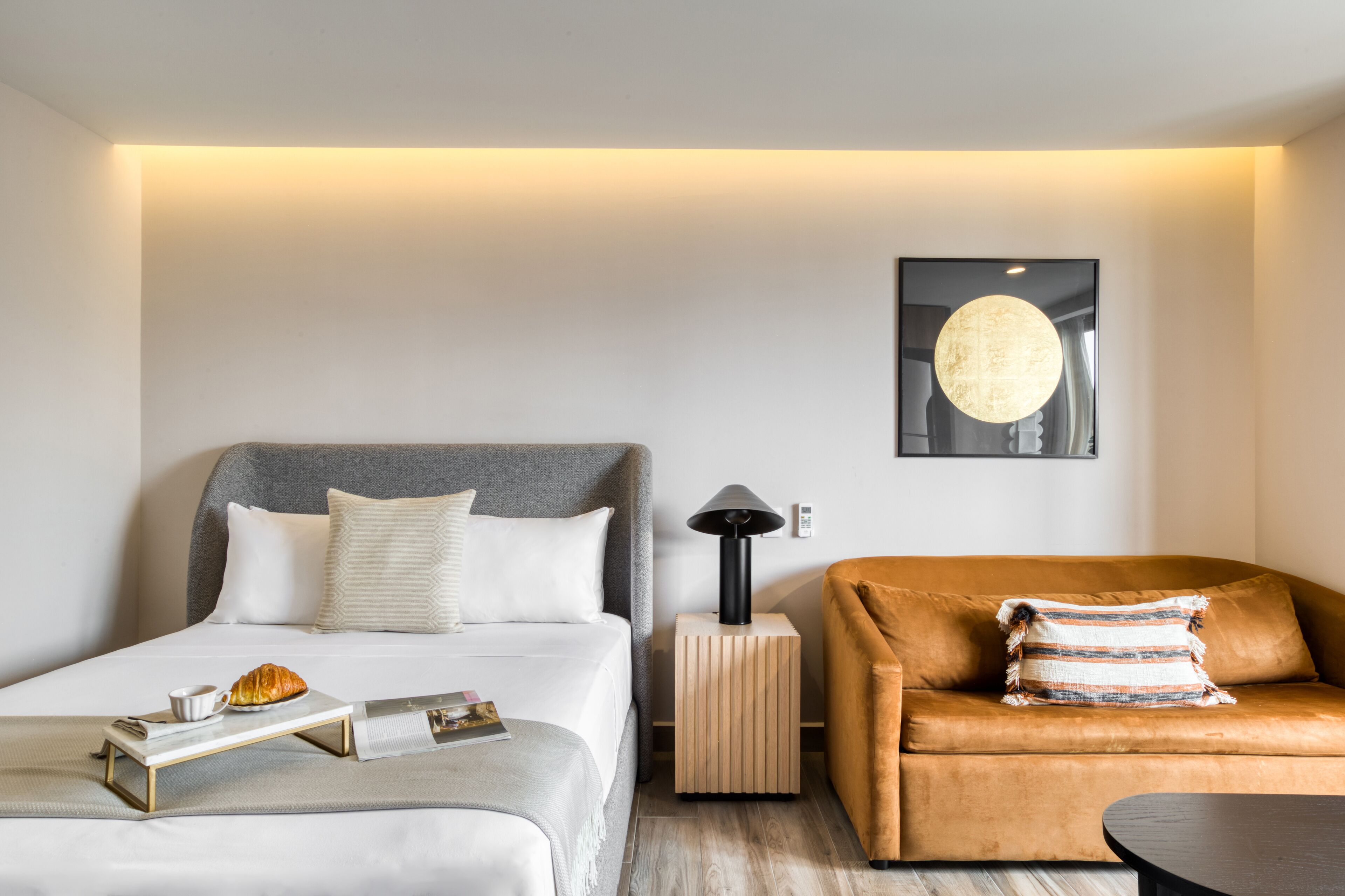 A modern hotel room with a bed, a sofa, a side table, and a lamp.