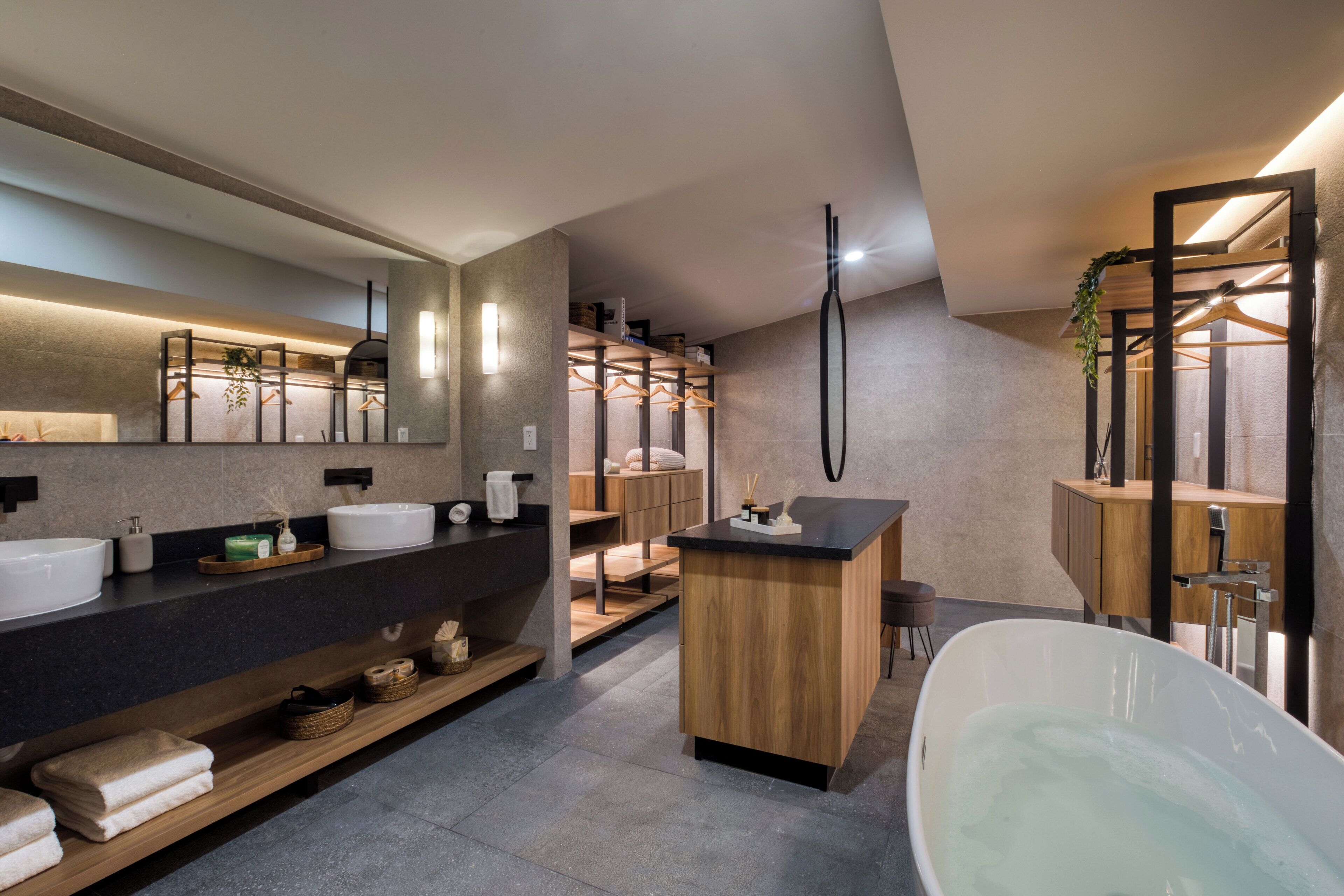 Un baño moderno con una bañera independiente, un espejo grande y un tocador de madera con lavamanos.