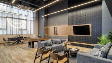 Un área de estar moderna con mesa de billar, sofás y sillones, que cuenta con un televisor grande y paneles acústicos en la pared.