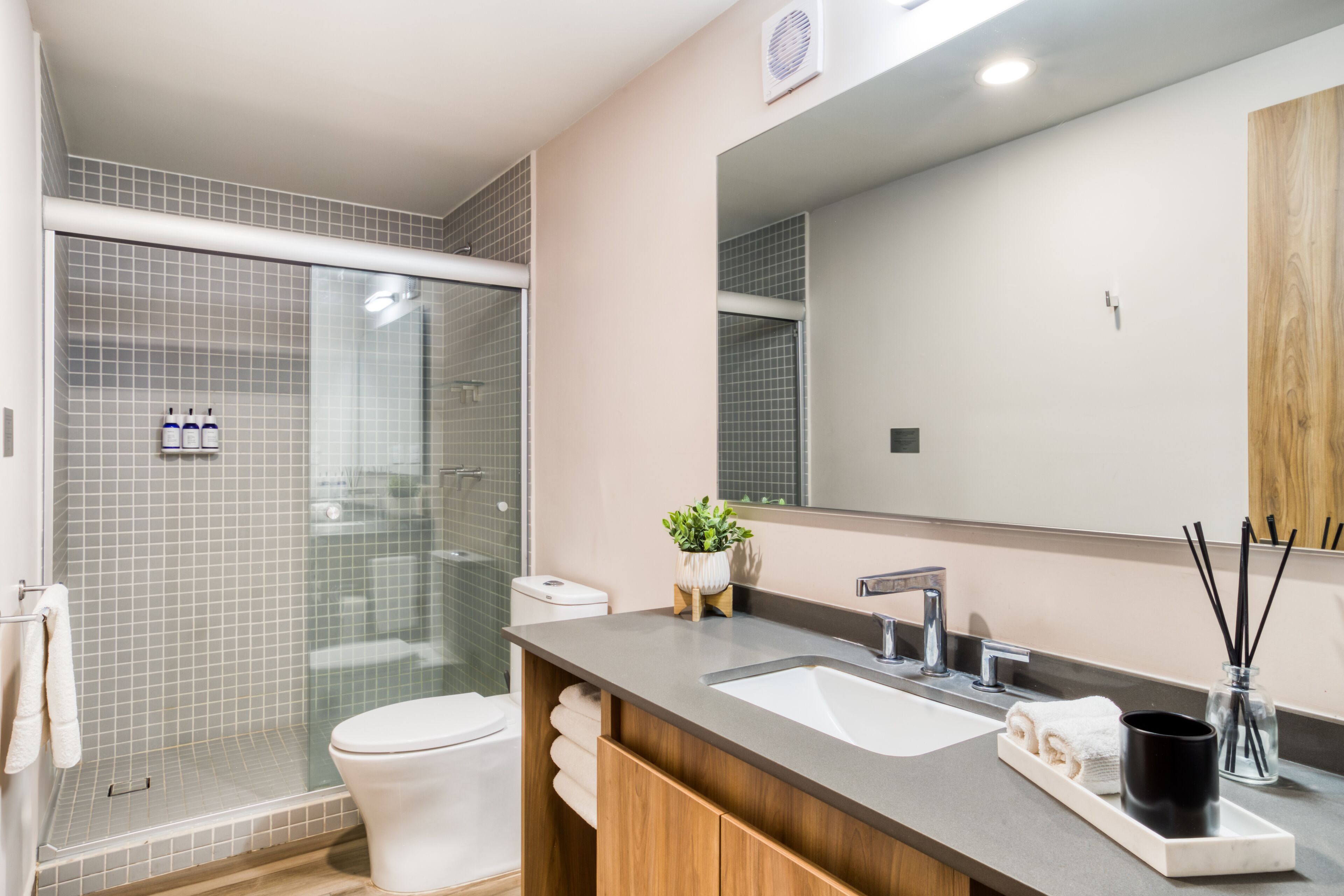 Un baño moderno con cabina de ducha de vidrio, inodoro blanco, espejo grande y lavabo de mármol.