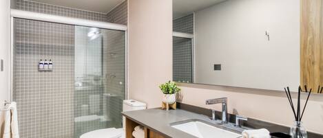 Un baño moderno con cabina de ducha de vidrio, inodoro blanco, espejo grande y lavabo de mármol.