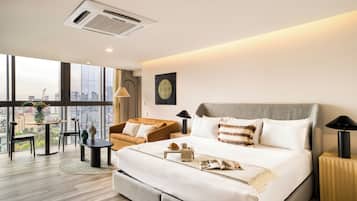 Una habitación de hotel moderna con una cama grande, una mesa de comedor redonda, un sofá y vistas a la ciudad.