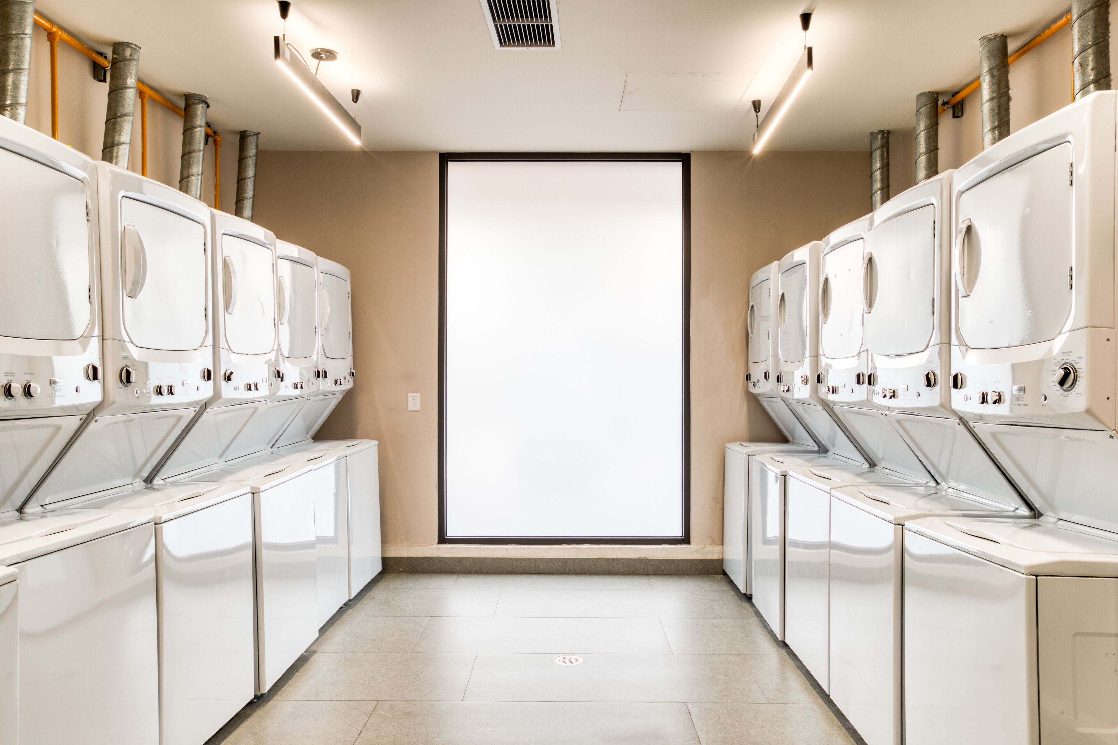 A row of white laundry machines with a large window in the center.