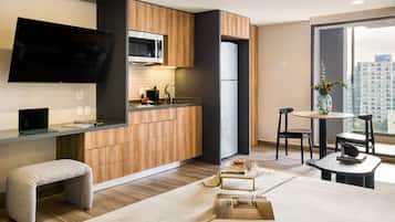 Cocina moderna con armarios de madera, microondas y refrigerador. Hay un comedor con mesa y sillas, y un ventanal que ofrece vistas de la ciudad.