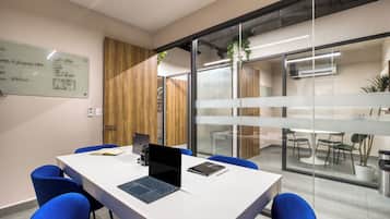 Una sala de reuniones moderna con una mesa blanca, sillas azules, una computadora portátil y una pizarra con texto.