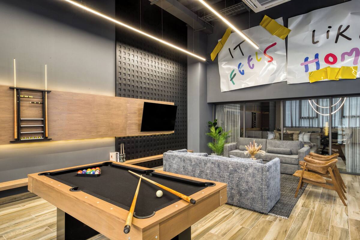 A modern lounge area with a pool table, comfortable seating, and a large TV screen.