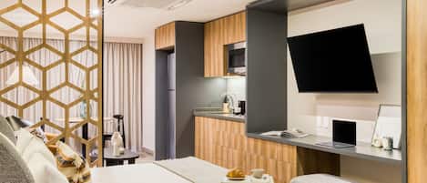 Una habitación de hotel moderna con cama, escritorio con computadora portátil, televisor de pantalla plana y una zona de kitchenette.