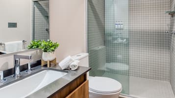 A modern bathroom with a glass-enclosed shower, a sink with a wooden cabinet, and a toilet.