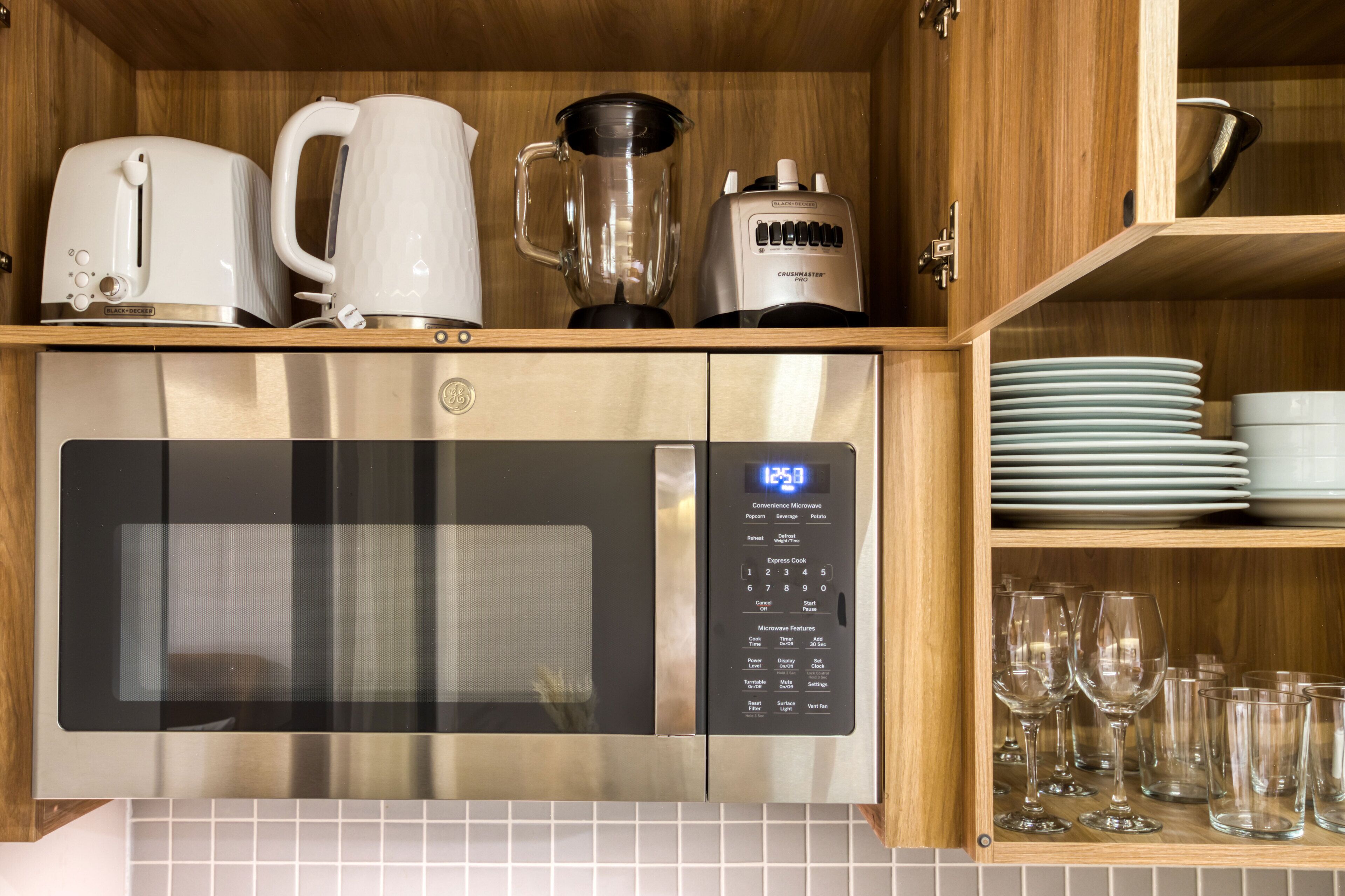 Una cocina con microondas de acero inoxidable, cafetera, licuadora y una pila de platos y vasos.