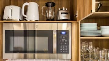 Una cocina con microondas de acero inoxidable, cafetera, licuadora y una pila de platos y vasos.