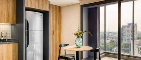 Eine moderne Küche mit einem Edelstahl-Kühlschrank, Holzschränken, einem runden Esstisch mit zwei Stühlen und einem großen Fenster mit Blick auf die Stadt.