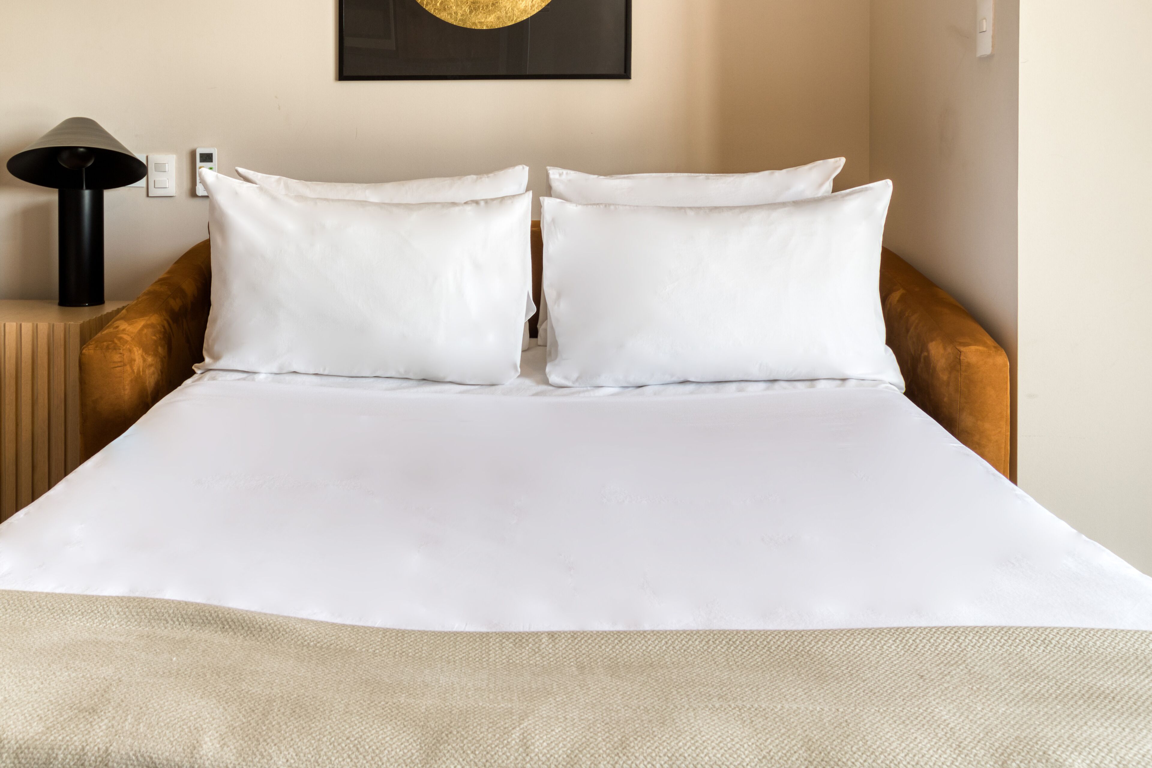 A neatly made bed with white linens, a brown upholstered headboard, and a single bedside lamp.
