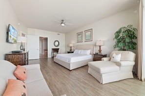 Habitación de hotel con cama, sofá, sillón, escritorio, lámpara, planta y ventilador de techo.