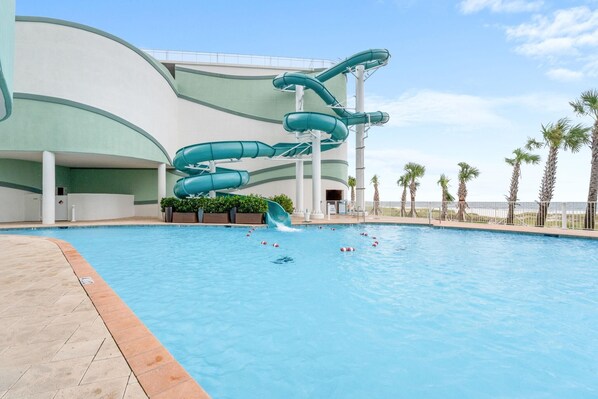 Una piscina con un tobogán de varios niveles y palmeras al fondo.