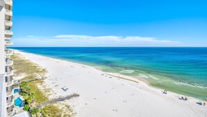 Ein Strand mit klarem, blauem Wasser, einem sandigen Ufer und einem Gebäude mit Balkonen mit Blick auf den Strand.