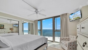 A bedroom with a large bed, a ceiling fan, a TV, and a view of the beach. - Perdido Towers West 908 (Pensacola)