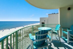 Un balcon avec vue sur la plage et l’océan. Il y a deux chaises et une table.