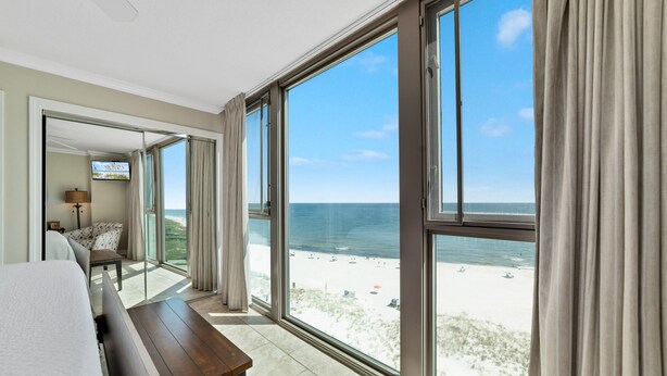 A hotel room with a large balcony, a bed, a wooden table, and a TV. - Perdido Towers West 908 (Pensacola)