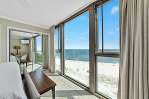 A hotel room with a large balcony, a bed, a wooden table, and a TV. - Perdido Towers West 908 (Pensacola)