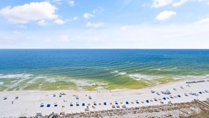 A beach with clear skies, calm waters, and rows of blue beach chairs and umbrellas. - Indigo East 1405 (Pensacola)