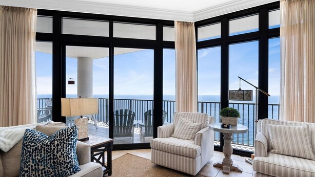 A spacious balcony with a view of the sea, furnished with a sofa, armchairs, and a small table with a lamp.