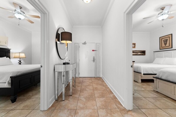 A hotel room with two beds, a vanity with a mirror, a ceiling fan, and a door with a red lock. - The Oasis at Orange Beach 2208 (Orange Beach)